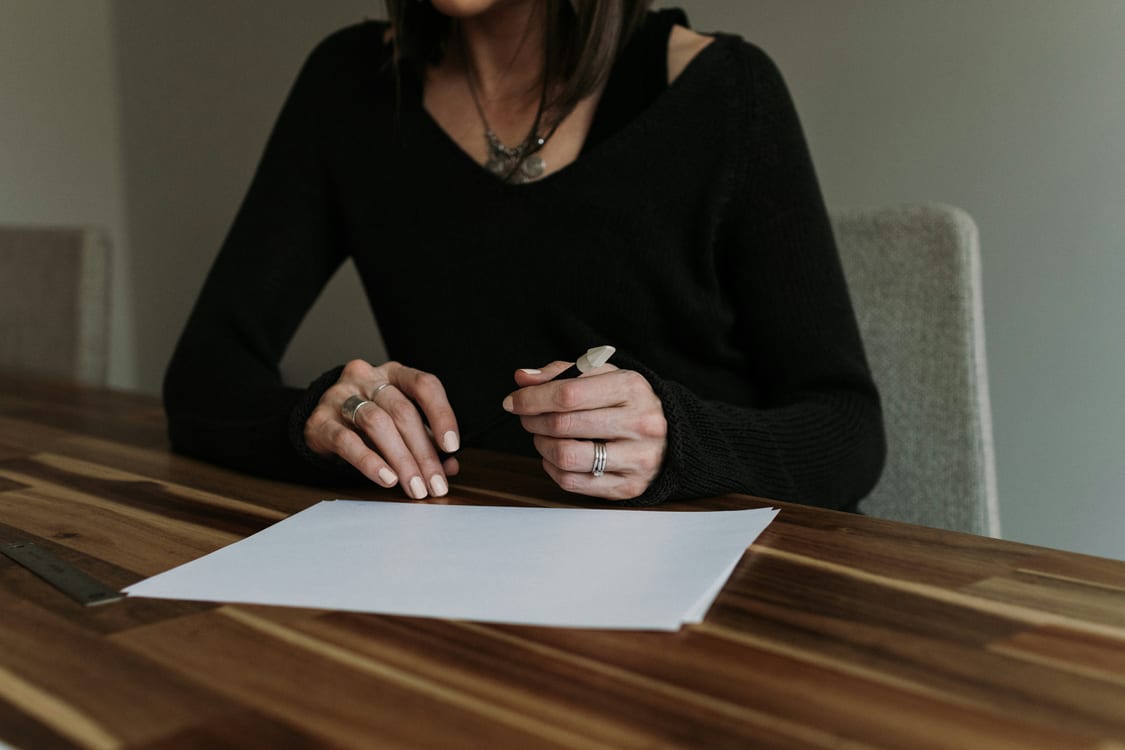 Mujer sentada frente a un papel sobre una mesa de madera, a punto de firmar el contrato de alquiler