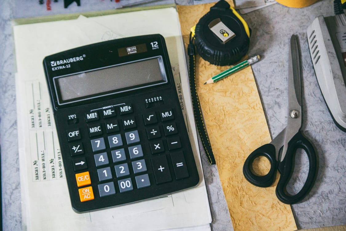 Calculadora sobre papel con cálculos manuscritos y cinta métrica para fijar el precio del alquiler