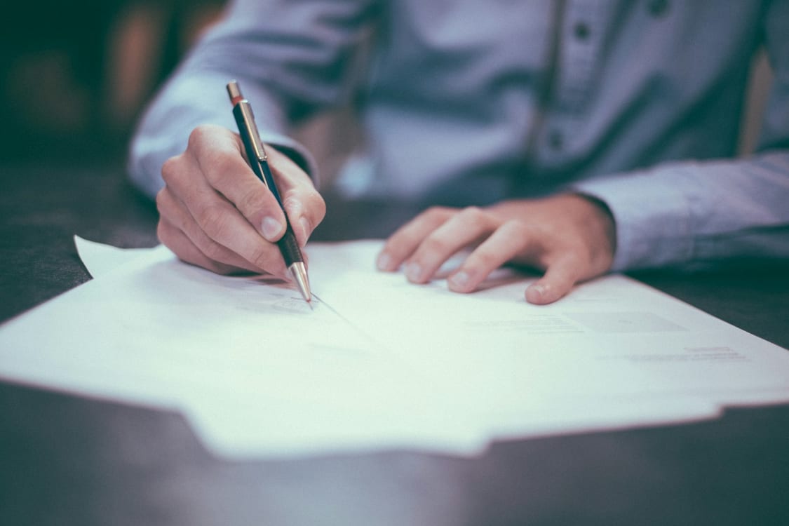 Persona firmando un contrato con un bolígrafo sobre una mesa oscura
